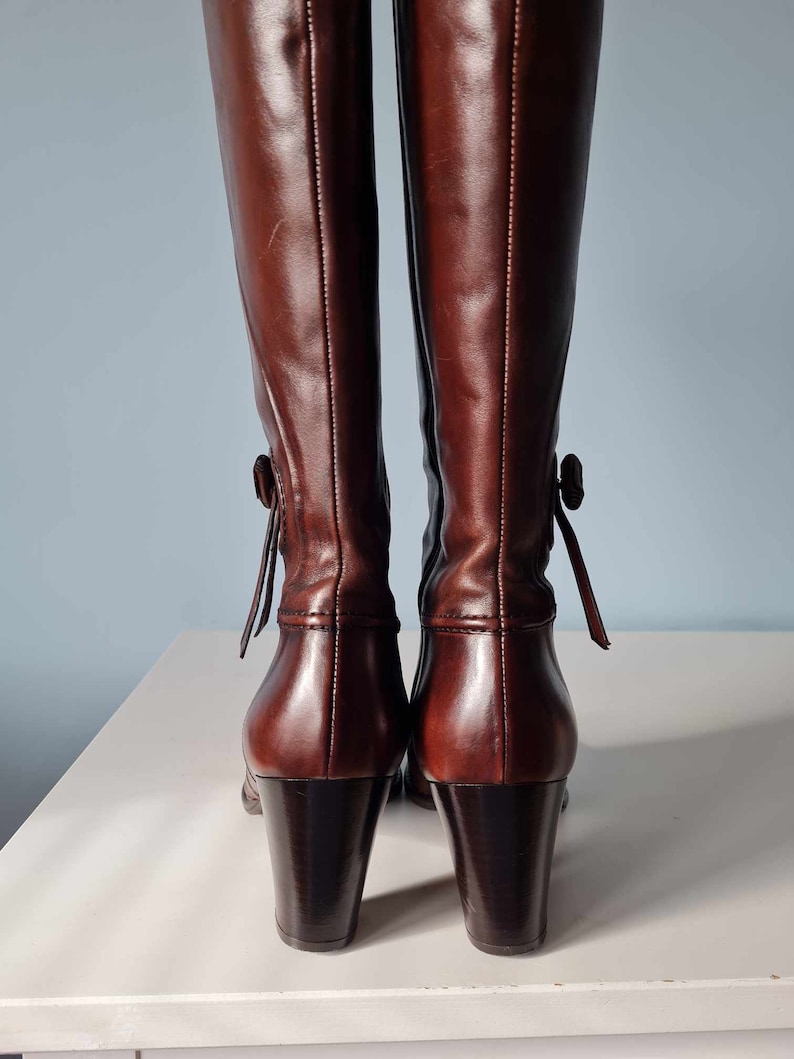 May include: A pair of brown leather knee-high boots with a block heel and a decorative tie at the back of the ankle.