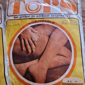 May include: A pack of nude heel stockings with adjustable straps. The packaging is yellow and orange with the text "Aristoc Tops for perfect fit without suspenders Adjustable" and "Bas Clair - Extensible Sans Jarretelles" and "Tient Out Seul Ne Fait Aucun Pli Monte Tres Haut". The pack also includes the text "B 9" - 10" 100% Nylon Exclusive of Garter Nude Heel".