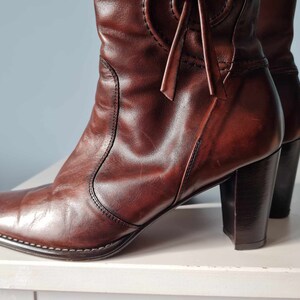 May include: A pair of brown leather heeled boots with a pointed toe and a decorative tie at the top of the shaft.