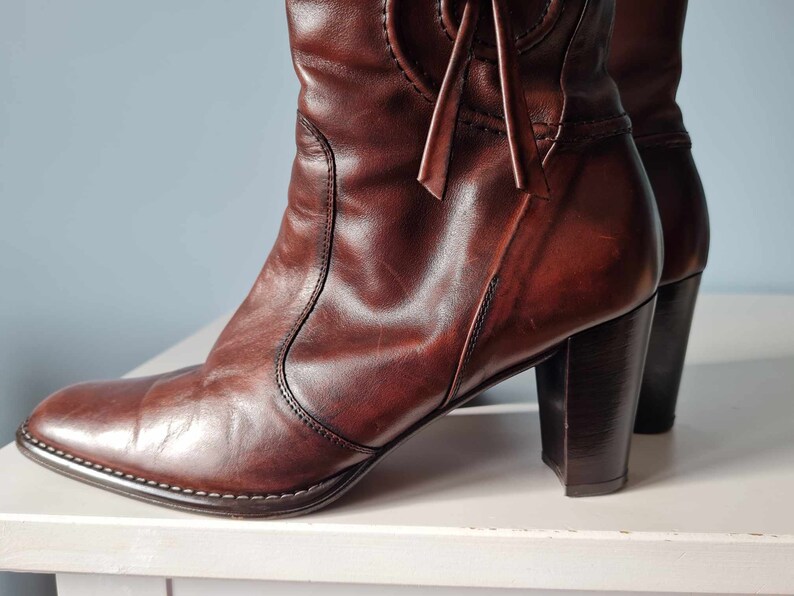 May include: A pair of brown leather heeled boots with a pointed toe and a decorative tie at the top of the shaft.