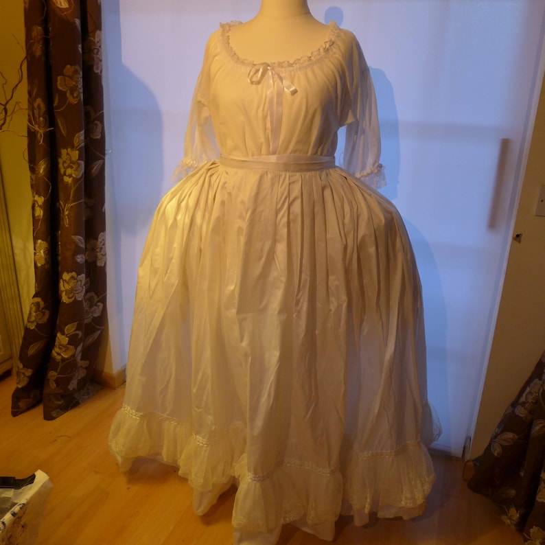 Puede incluir: Un vestido blanco largo con ribete de encaje y falda fruncida. El vestido tiene un corpi&ntilde;o ajustado con escote de encaje y una cinta atada a la cintura.