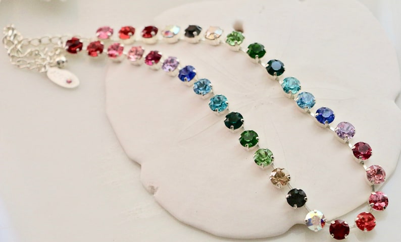 Puede incluir: Un collar de cadena de plata con cuentas de cristal de colores arco&iacute;ris. El collar est&aacute; sobre un fondo blanco.