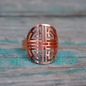 Può includere: Un anello in rame con un design circolare che presenta un motivo geometrico. L'anello è realizzato in un unico pezzo di metallo e ha una finitura liscia e lucida.