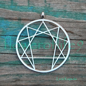 Peut inclure: Pendentif en argent avec un motif géométrique comprenant une étoile à sept branches à l'intérieur d'un cercle. Le pendentif est sur une surface en bois.