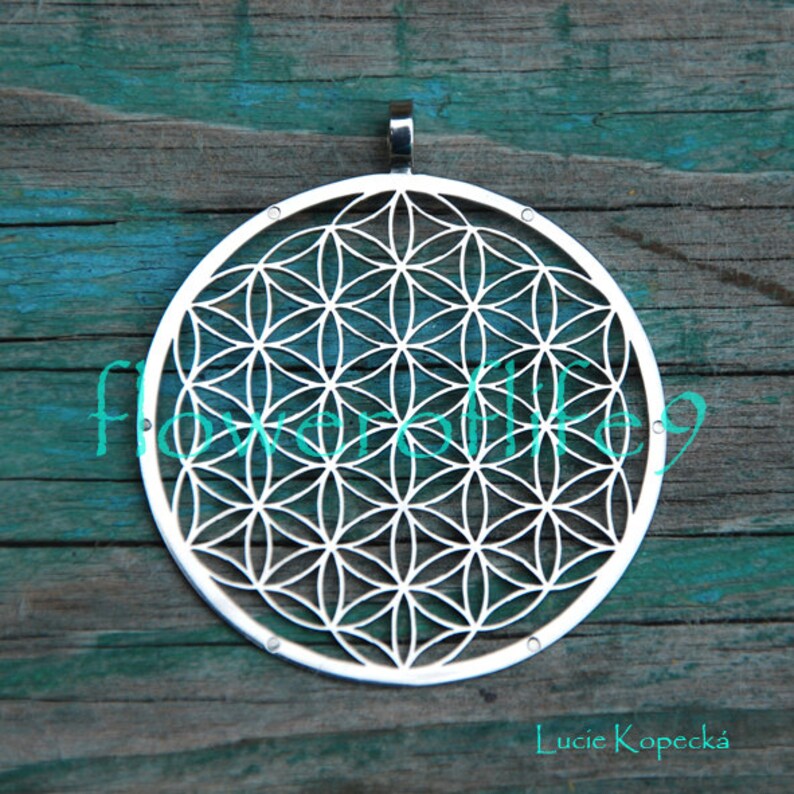 May include: A silver pendant featuring a detailed geometric design known as the Flower of Life. The pendant is round and has a smooth, polished finish.