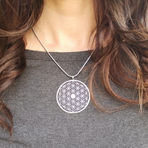 May include: A silver necklace with a round pendant featuring a geometric flower of life design.