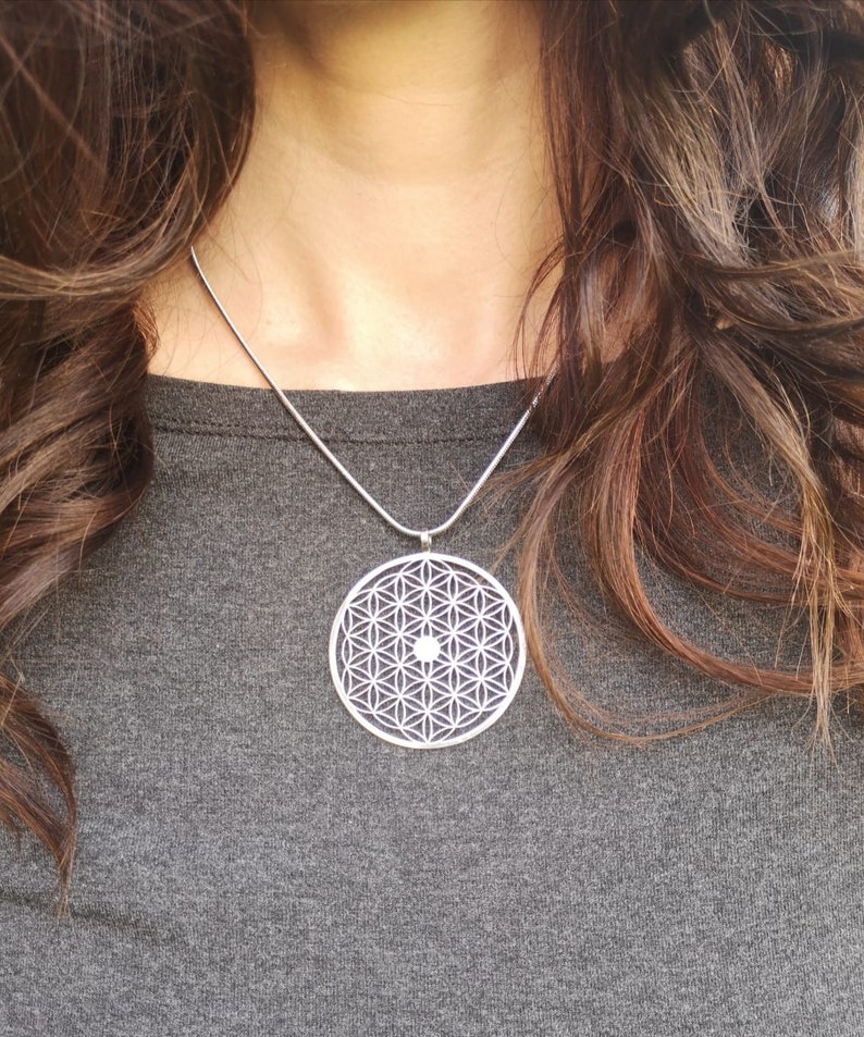 May include: A silver necklace with a round pendant featuring a geometric flower of life design.