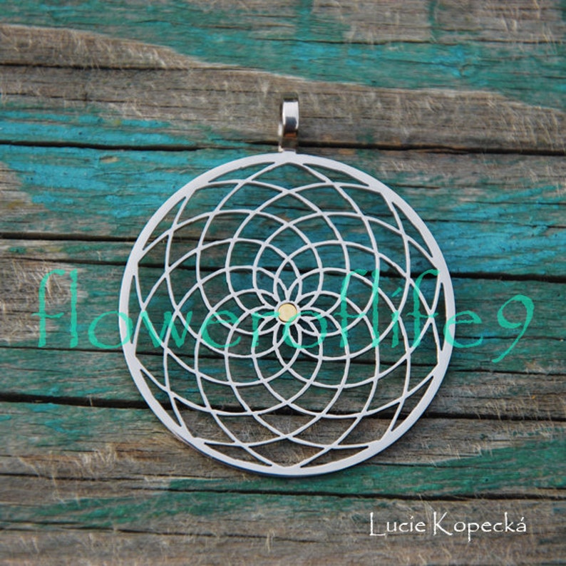 May include: A silver pendant with a geometric design resembling a flower of life. The pendant is circular and has a small gold dot in the center.