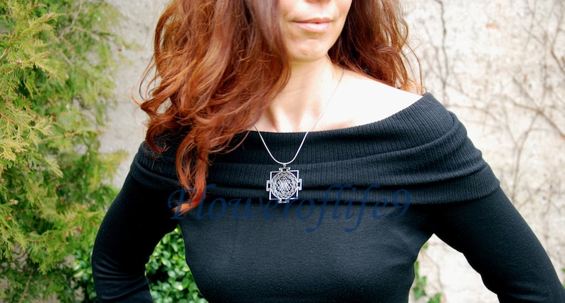 K&ouml;nnte beinhalten: Eine Frau tr&auml;gt einen schwarzen, schulterfreien Pullover mit einer silbernen Halskette mit einem geometrischen Anh&auml;nger.