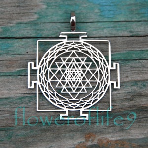 May include: Silver pendant featuring a Sri Yantra, a sacred geometric symbol in Hinduism. The pendant is intricately designed with a central star and multiple triangles.