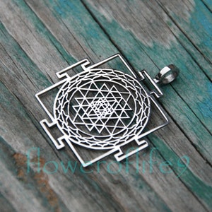 May include: A silver pendant featuring a Sri Yantra, a sacred geometric symbol in Hinduism, with intricate details and a loop for hanging.