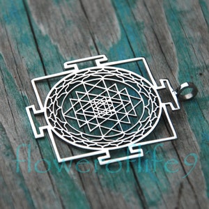 May include: A silver pendant featuring a Sri Yantra design, a sacred geometric symbol in Hinduism. The pendant is intricately detailed and has a circular shape with a square frame.