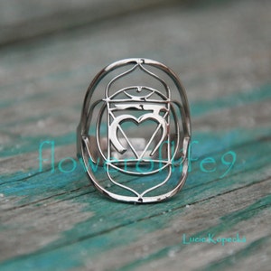 Op de afbeelding: Zilveren ring met een geometrisch ontwerp met een hart en het getal vijf. De ring is een symbool van de hartchakra.