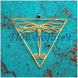 Puede incluir: Un colgante de metal dorado en forma de triángulo con un diseño de libélula en su interior. El colgante tiene un bucle en la parte superior para colgar. El texto "Floweroflife9" es visible en el fondo.