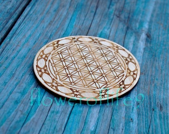 Könnte beinhalten: Ein runder Holz-Untersetzer mit einem lasergravierten geometrischen Muster, bekannt als Blume des Lebens, in hellbrauner Farbe.