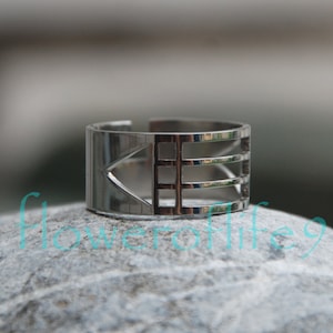 Puede incluir: Un anillo de plata con un diseño geométrico que presenta un triángulo y tres barras horizontales.