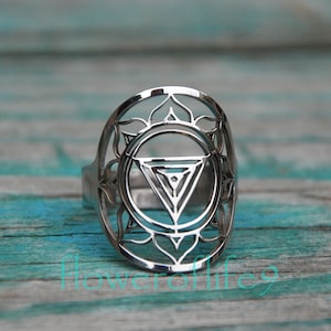 May include: A silver ring with a detailed design of a chakra symbol. The ring is made of metal and has a circular shape.