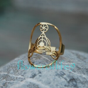 May include: Gold ring with a geometric design featuring a circle within a triangle. The ring is made of metal and has a polished finish.
