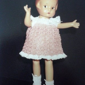 May include: A vintage porcelain doll with red hair wearing a pink crocheted dress with white lace trim and white shoes.