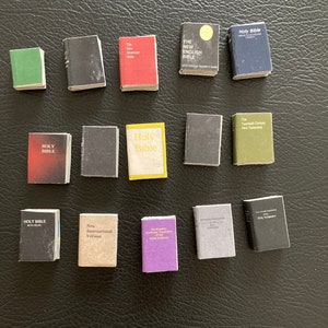 May include: A collection of miniature books, including various versions of the Holy Bible, the New English Bible, the New International Version, and the New Testament. The books are all different colors and sizes, and some have gold lettering.