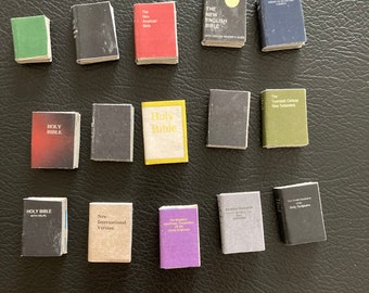 May include: A collection of miniature books, including various versions of the Holy Bible, the New English Bible, the New International Version, and the New Testament. The books are all different colors and sizes, and some have gold lettering.