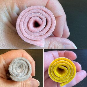 May include: Three separate rolls of felt material shown in individual close-up views. One roll is light pink, one is a neutral heathered gray, and one is a vibrant yellow. Each roll displays a spiral pattern created by the layered felt fabric.