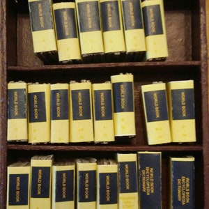 May include: A set of 26 miniature World Book Encyclopedia volumes in a wooden box. The books are yellow with blue spines and gold lettering. The volumes are numbered 1 through 26.