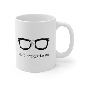 Op de afbeelding: Witte keramische mok met een zwart-witte afbeelding van een bril en de tekst "talk nerdy to me". De mok heeft een gebogen handvat en is geschikt voor warme of koude dranken.