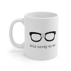 Op de afbeelding: Witte keramische mok met een zwarte brilomtrek en een witte band. De zin "talk nerdy to me" staat eronder in het zwart gedrukt. De mok heeft een gebogen handvat.