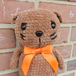 May include: A brown crocheted teddy bear with black eyes and a black nose. The bear is wearing an orange bow.