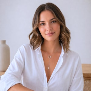 Op de afbeelding: Een zilveren ketting met een cirkelvormige hanger verbonden met een verticale staaf, eindigend met een halve maan bedel. De ketting wordt gedragen met een wit overhemd.