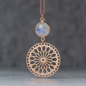 May include: A rose gold necklace with a round, white moonstone pendant and a delicate, circular filigree design.