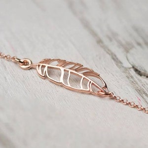 May include: A delicate rose gold chain bracelet with a delicate, openwork feather charm.