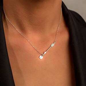 May include: A silver necklace with a small circle pendant and an arrow charm. The arrow charm is pointing to the right.