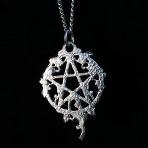 Puede incluir: Un collar de plata con un colgante de pentagrama. El colgante es una estrella de cinco puntas con un dise&ntilde;o detallado y ornamentado.