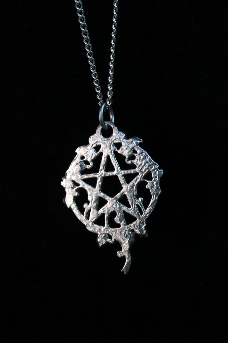 Puede incluir: Un collar de plata con un colgante de pentagrama. El colgante es una estrella de cinco puntas con un dise&ntilde;o detallado y ornamentado.