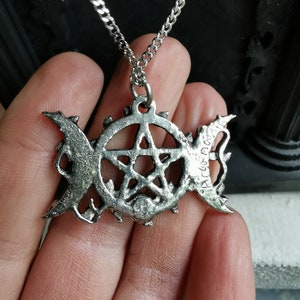 May include: A silver necklace with a pentagram pendant featuring a triple moon symbol and the inscription "ART & CRAFT".