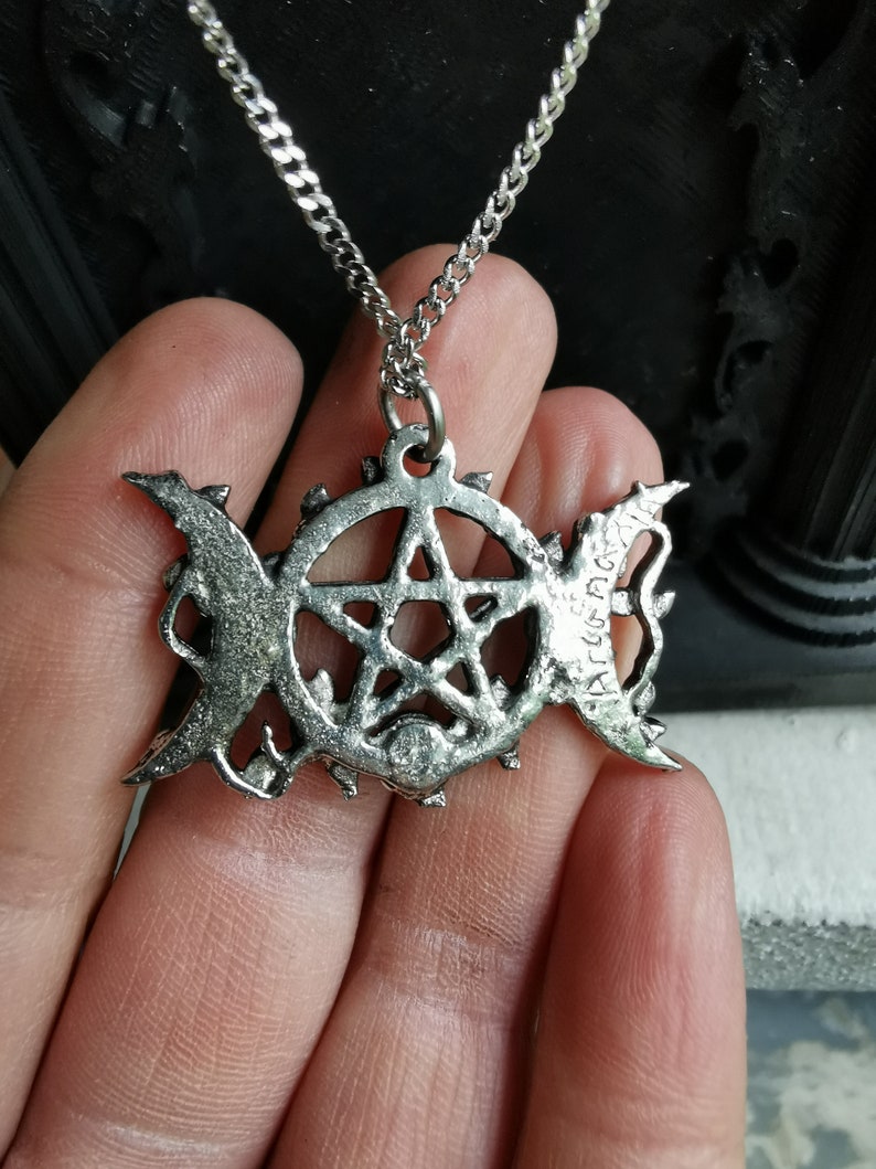 May include: A silver necklace with a pentagram pendant featuring a triple moon symbol and the inscription "ART & CRAFT".