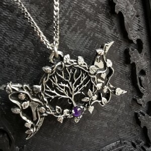 May include: A silver necklace with a pendant featuring a detailed tree of life design with leaves and a purple gemstone in the center.