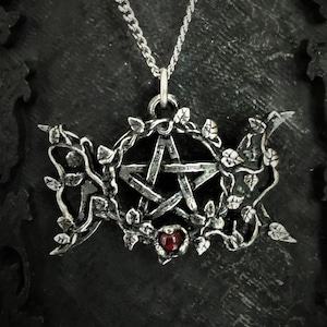 May include: A silver pendant necklace featuring a pentagram surrounded by vines and a red gemstone. The necklace is on a silver chain.