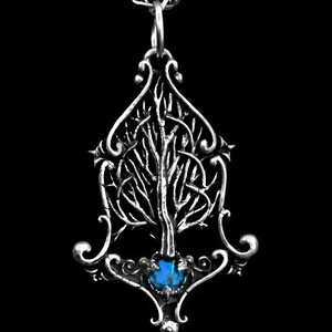K&ouml;nnte beinhalten: Eine silberne Halskette mit einem detaillierten Baumdesign und einem blauen Edelstein an der Basis. Der Anh&auml;nger ist an einer silbernen Kette befestigt.
