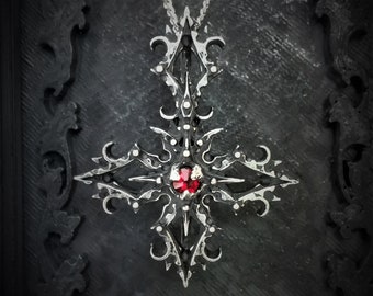 Puede incluir: Un collar con un colgante de plata con un diseño de estrella grande e intrincado. El colgante tiene una piedra preciosa roja en el centro.