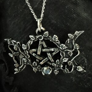 May include: Silver pendant necklace featuring a pentacle with a moonstone in the center, surrounded by a vine design.
