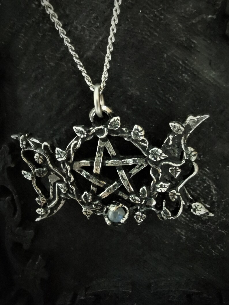 May include: Silver pendant necklace featuring a pentacle with a moonstone in the center, surrounded by a vine design.