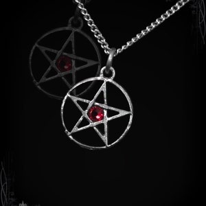 May include: A silver chain necklace with two pentagram pendants. Each pendant features a red gemstone in the centre.