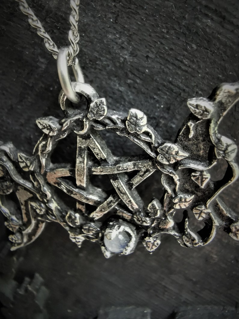 May include: A silver pendant necklace with a pentagram design surrounded by leaves and a clear gemstone. The necklace is on a silver chain.