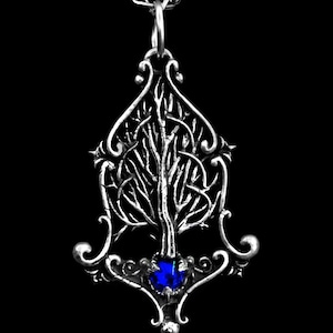 K&ouml;nnte beinhalten: Eine silberne Halskette mit einem Anh&auml;nger, der ein detailliertes Baumdesign mit einem blauen Edelstein an der Basis zeigt. Der Baum ist von filigranen Schn&ouml;rkeln umgeben.