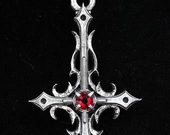 Könnte beinhalten: Eine silberne Halskette mit einem detailreichen, umgekehrten Kreuz-Anhänger. Das Kreuz hat einen roten Edelstein in der Mitte.