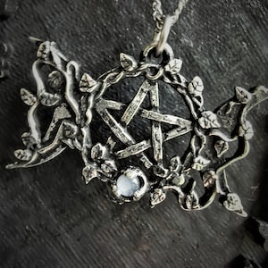 May include: A silver pendant necklace with a pentagram charm surrounded by a vine design. The pentagram has a clear gemstone in the center.