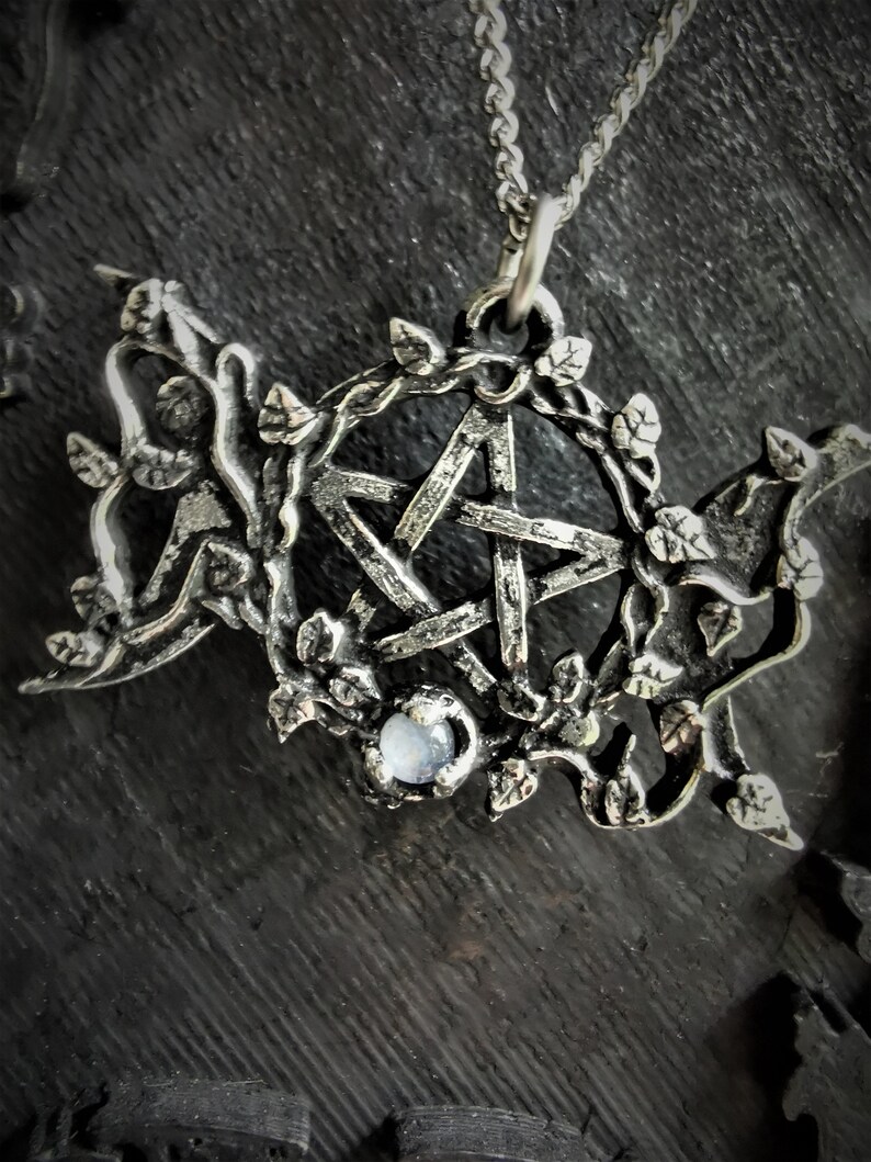 May include: A silver pendant necklace with a pentagram charm surrounded by a vine design. The pentagram has a clear gemstone in the center.